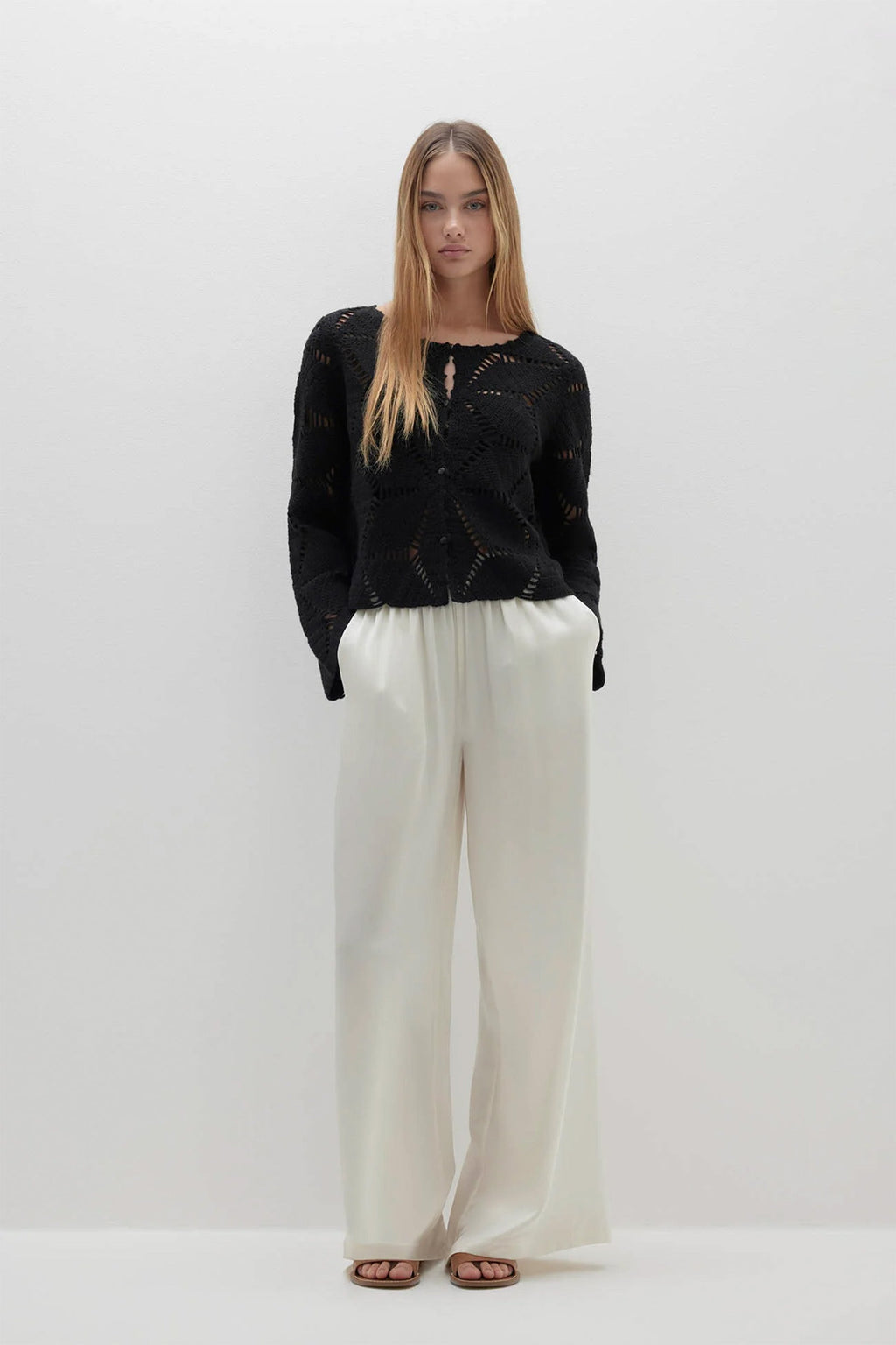 Woman wearing a black sweater and white pants on a white background