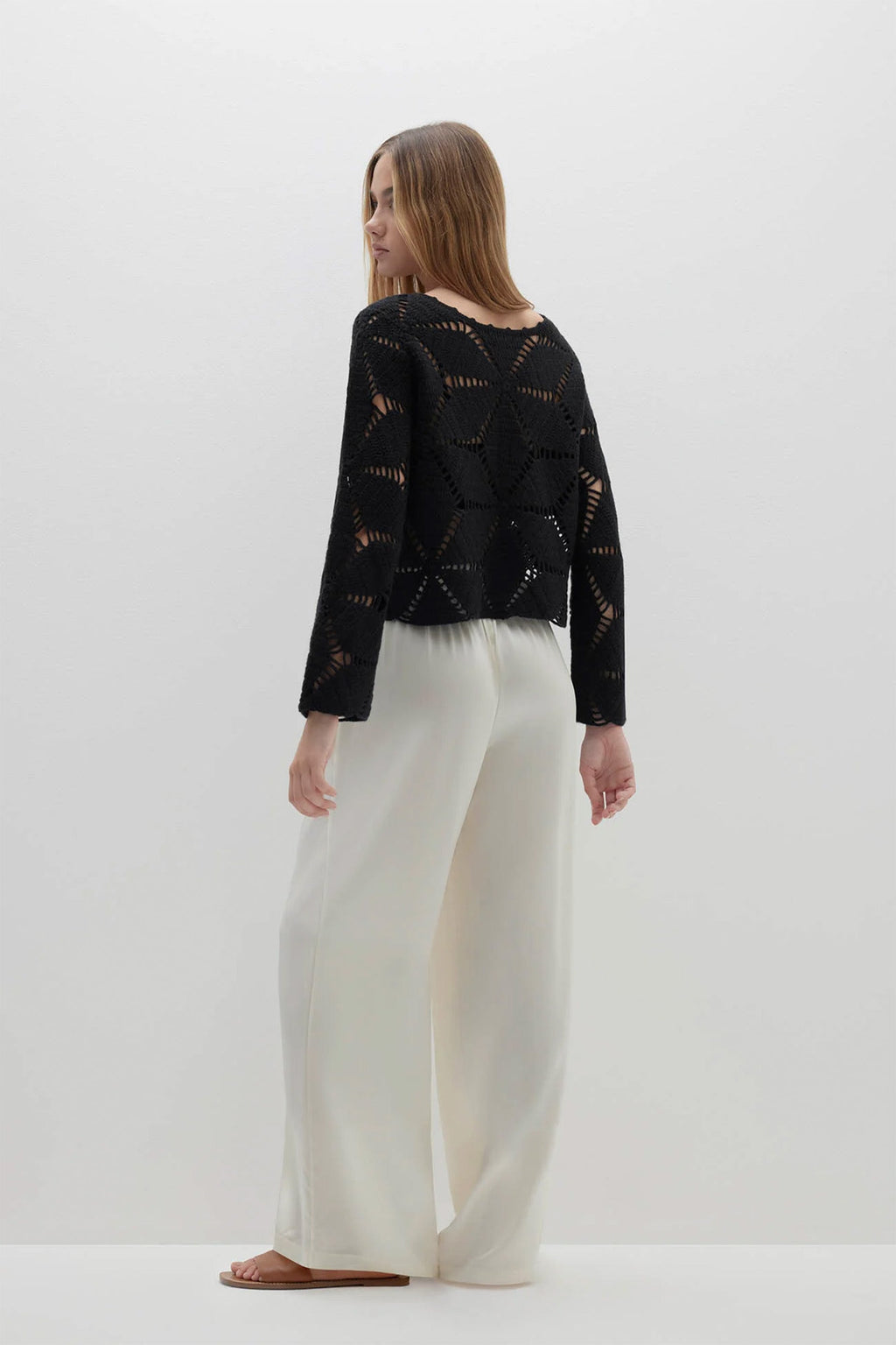 Woman wearing a black patterned top and white pants on a white background